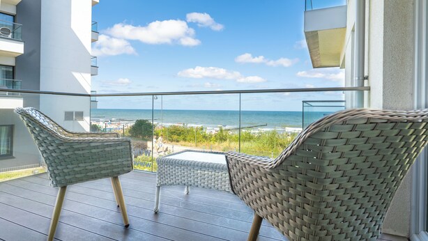 A balcony with wicker chairs, a glass balustrade, and a view of the beach and ocean. - Apartamenty Sun&Snow Przy Plaży (Mielno)
