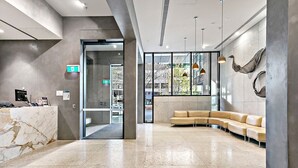 Un espace d’accueil moderne avec un comptoir de réception en marbre, un canapé incurvé de couleur beige et des luminaires suspendus.