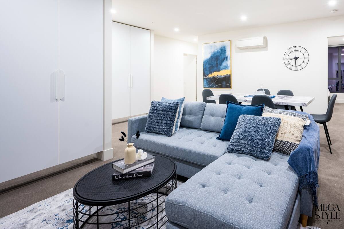 A modern living room with a grey sectional sofa, a coffee table, and a dining area with a white table and chairs.