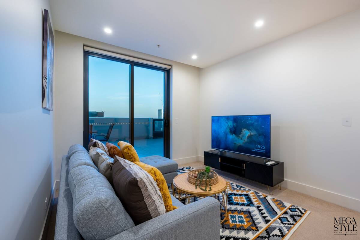 A modern living room with a grey sofa, a flat-screen TV, and a large window.