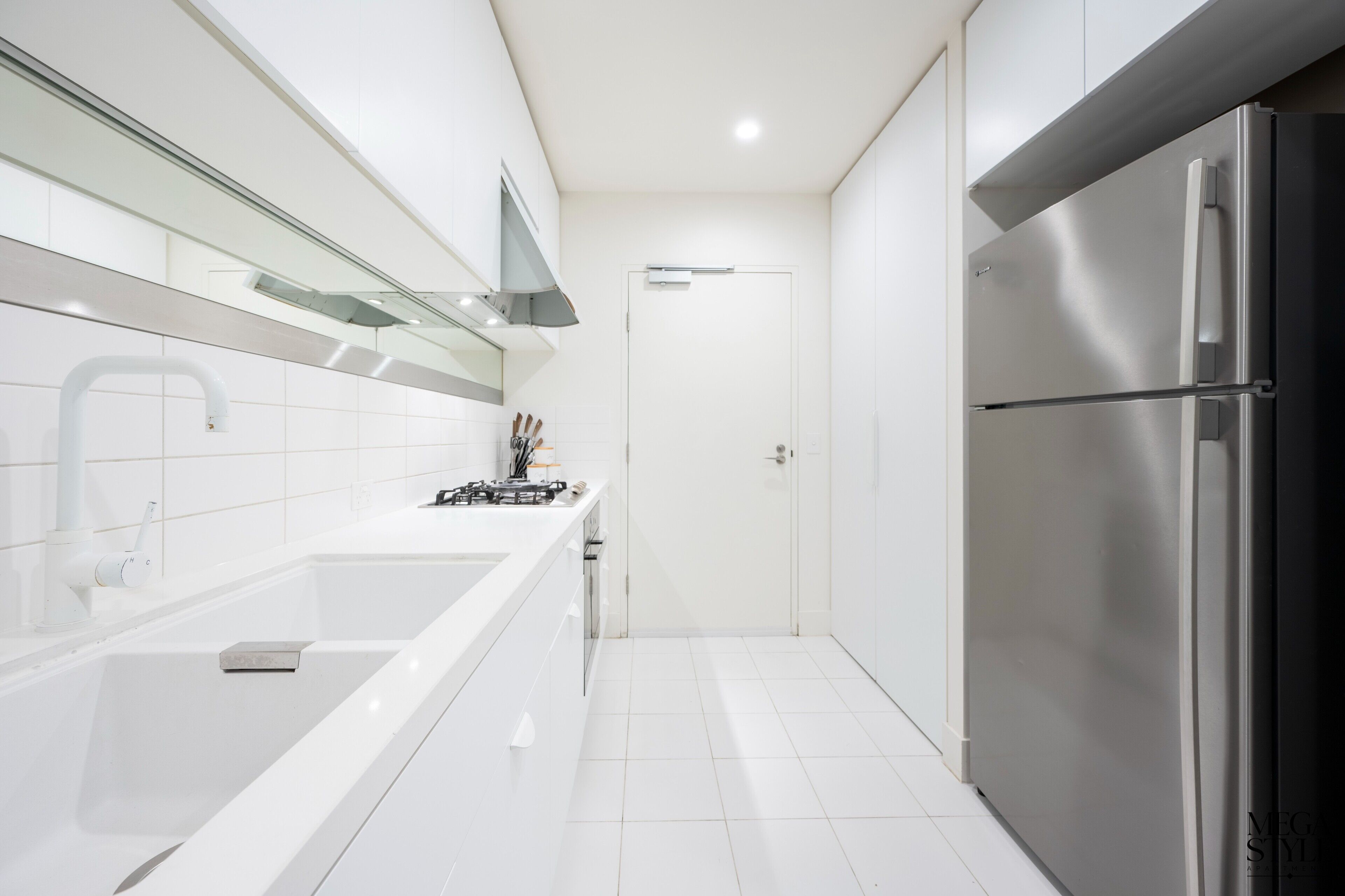 A modern kitchen with white cabinetry, a stainless steel refrigerator, and a white sink.