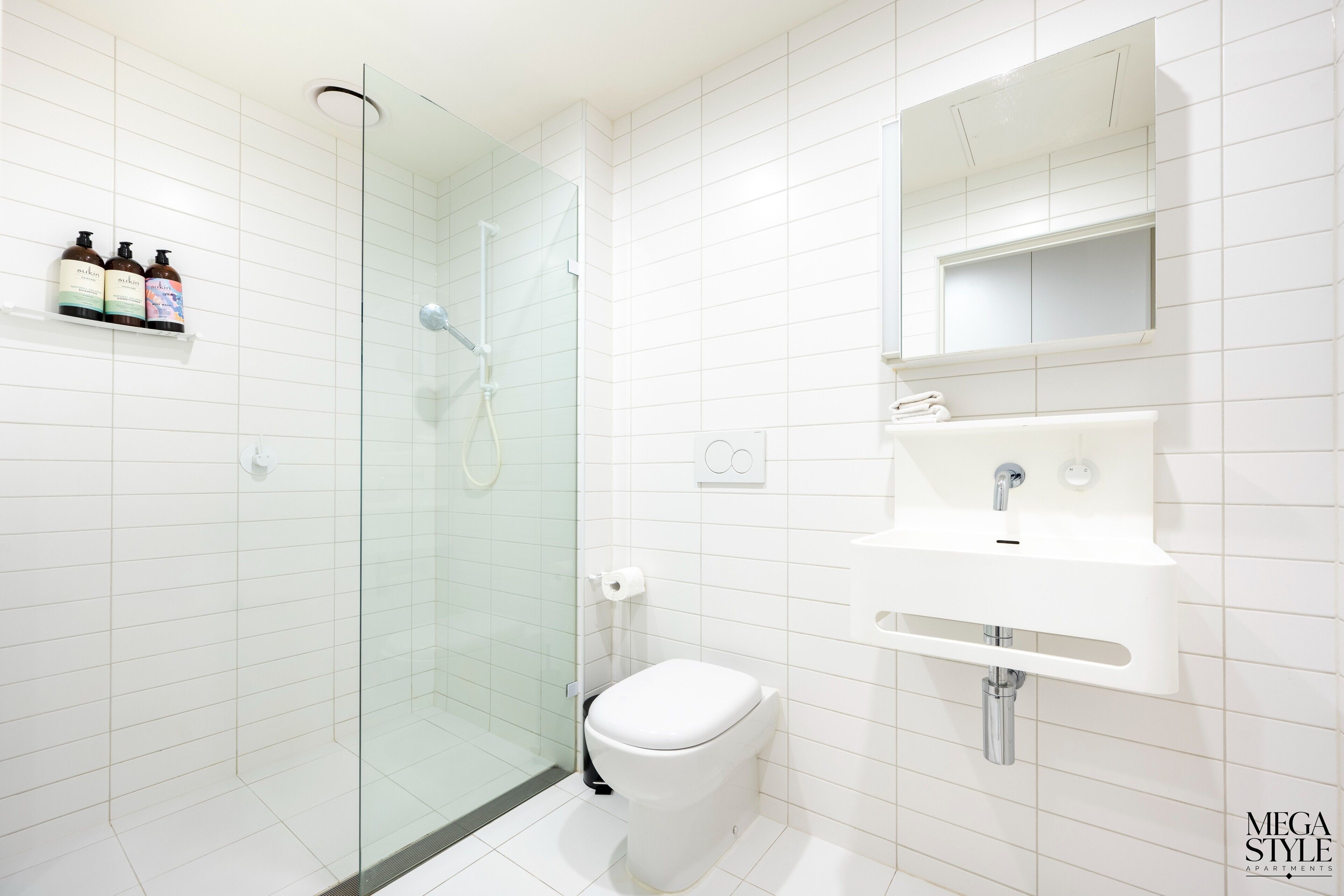 Een moderne badkamer met een douchecabine van glas, een wit toilet en een wastafel met spiegel erboven.