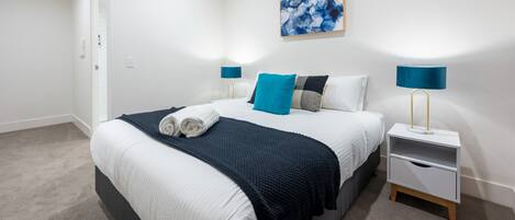 Ein modernes Schlafzimmer mit einem ordentlich bezogenen Bett, einem blauen abstrakten Gemälde und einem Nachttisch mit Lampe.