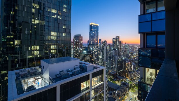 Un immeuble de grande hauteur doté d’une terrasse sur le toit, entouré d’autres bâtiments imposants et offrant une vue sur le paysage urbain au crépuscule.