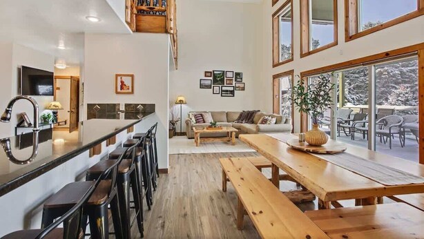 Een ruime woonkamer met een houten bank, een eettafel en een keuken met een barstoel.