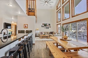 A spacious living area with a wooden bench, a dining table, and a kitchen area with a bar stool. - Lake House In Cascade w/ Hot Tub (Cascade)