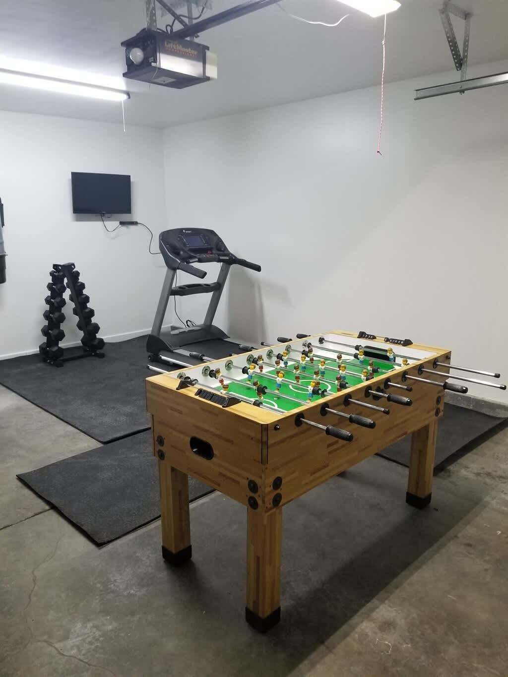 Une pièce équipée d’un baby-foot, d’un tapis de course et d’un projecteur fixé au plafond.