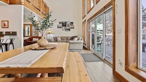 Een ruime woonkamer met een houten eettafel, een bank en een groot raam met uitzicht op de omgeving.