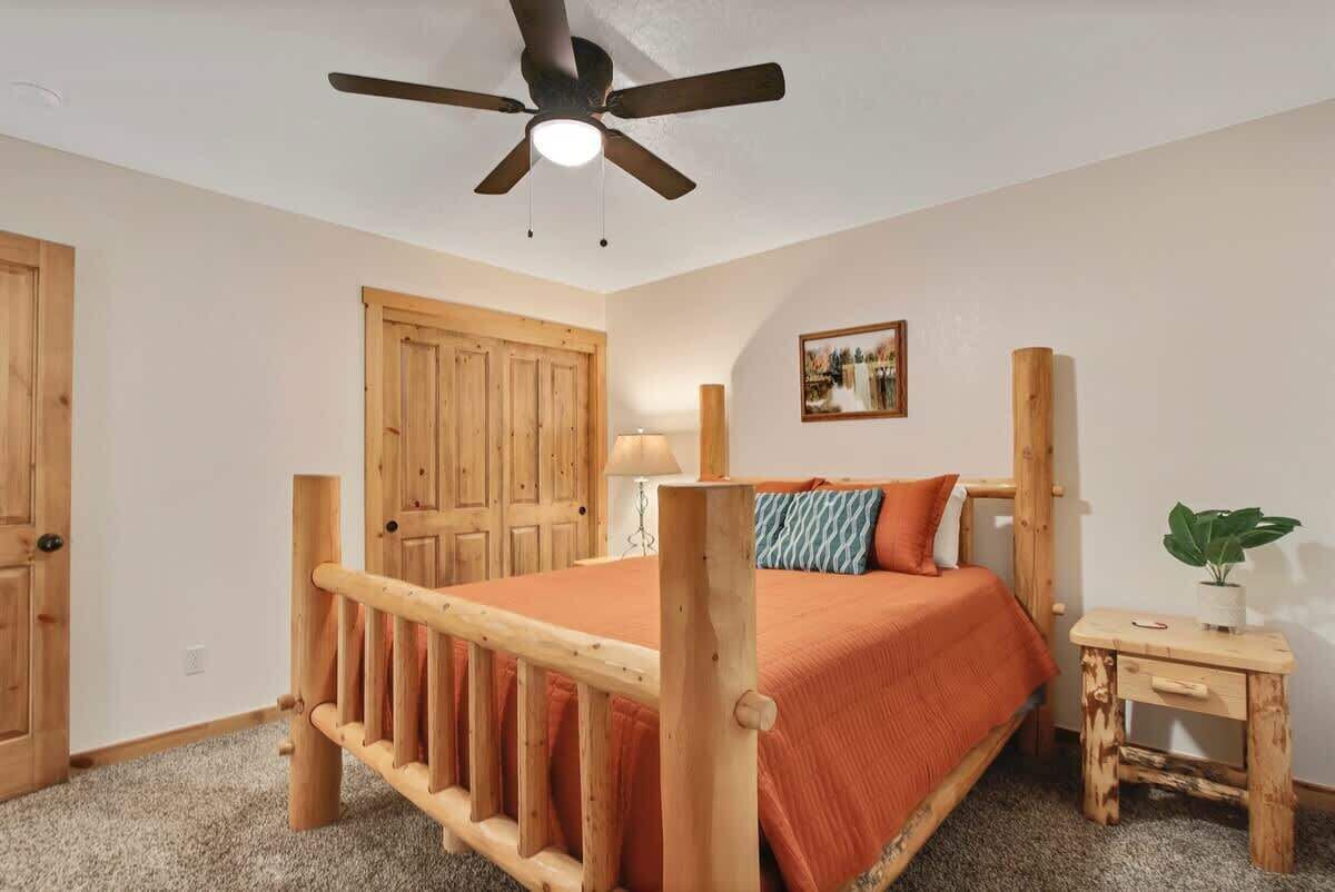 Een slaapkamer met een houten bedframe, een plafondventilator, een houten deur en een klein nachtkastje met een plant.