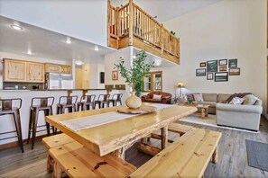 A spacious living area with a wooden dining table, benches, a sofa, and a staircase leading to an upper level. - Lake House In Cascade w/ Hot Tub (Cascade)