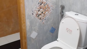 A bathroom with a white toilet, a shower area with a handheld showerhead, and a tiled wall with a decorative pebbles pattern.