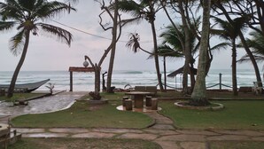 A beachside patio with palm trees, a wooden boat, and a stone pathway leading to a seating area.
