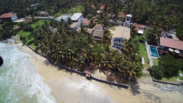 An aerial view of a coastal residential area with houses, palm trees, and a beach.