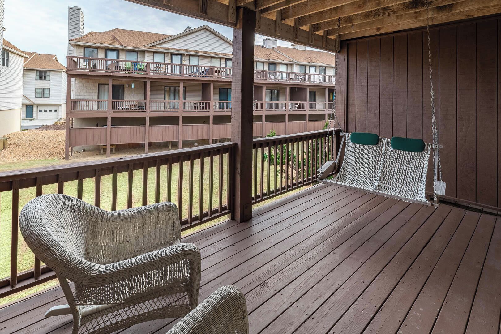 A wooden deck with wicker chairs and a hammock, overlooking a residential building with multiple balconies.