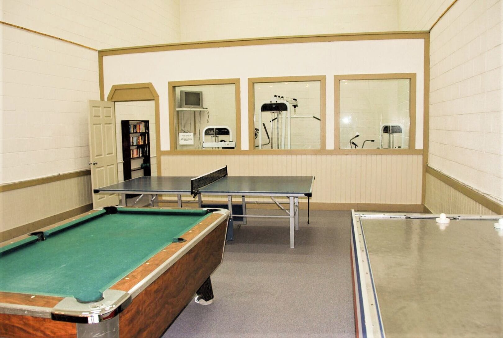 Una sala de billar con mesa de billar, mesa de ping pong y un muro espejado.
