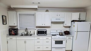 Una cocina moderna con armarios blancos, estufa a gas, microondas, fregadero y refrigerador.