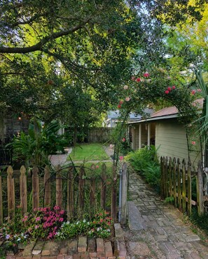 Ein Gartenweg führt zu einem Haus mit Holzzaun und blühenden Pflanzen.