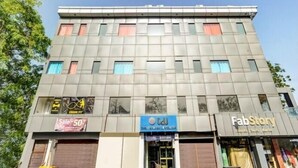 Un edificio de varios pisos con espacios comerciales en la planta baja, incluyendo una tienda con un cartel de 'Sale 50%' y otra con un letrero azul.
