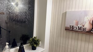 Finestra amb dibuixos de gel decoratius, una petita planta en test, un flascó de gel hidroalcohòlic i una estant amb la paraula “HOME” i una espelma.