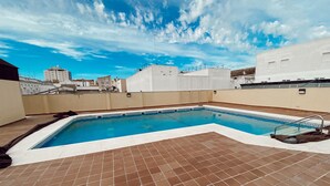 Ein Pool auf dem Dach mit blauem Himmel und Stadtansicht im Hintergrund.