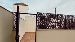 Eine Dachterrasse mit einem Metallgitter, einem Fliesenboden und einer Laterne.
