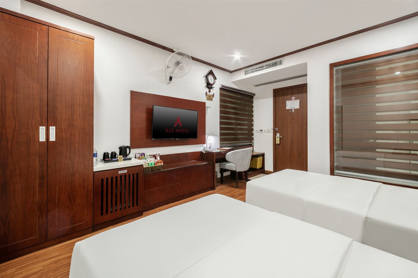 A hotel room with a wooden wardrobe, a desk with a computer, a TV, and two beds.