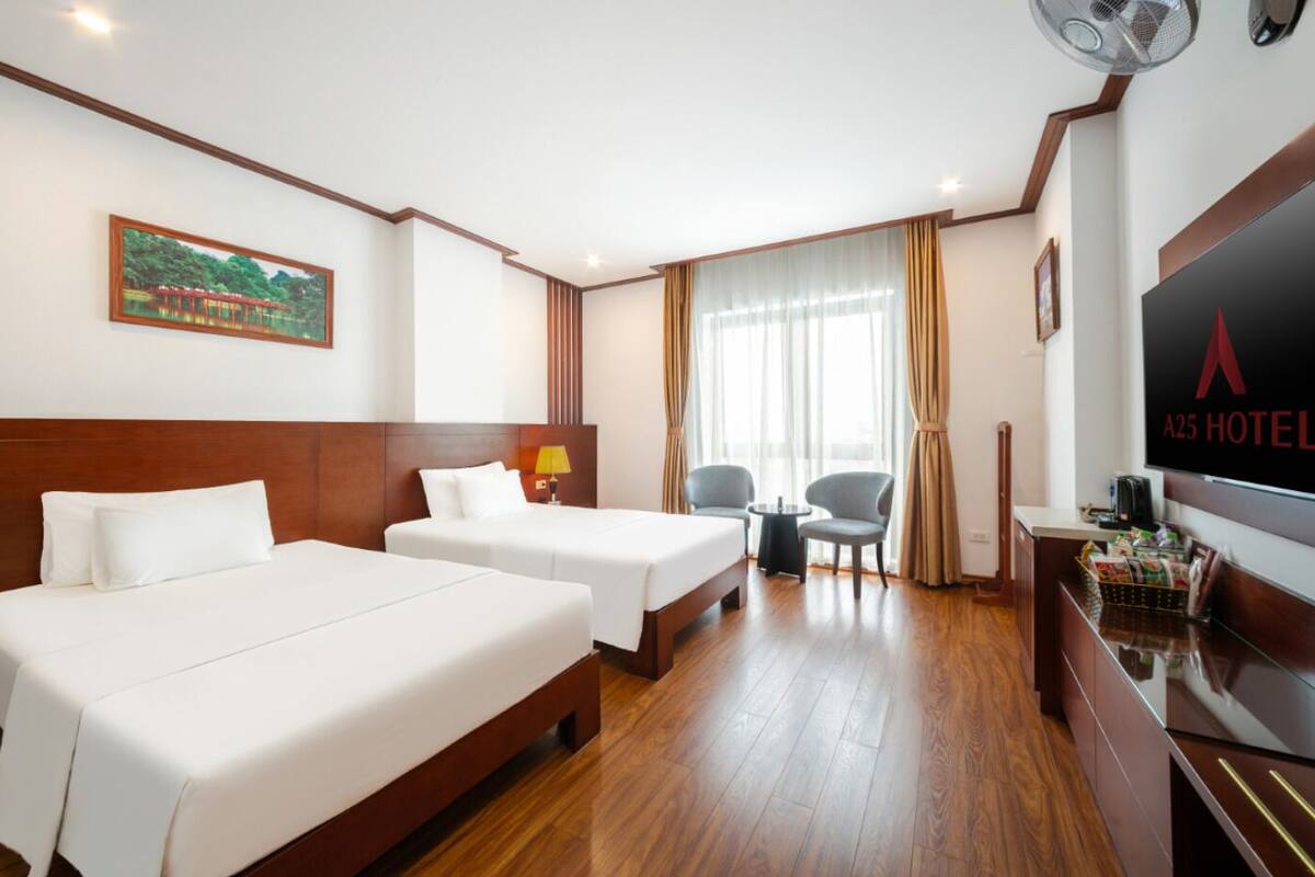 A hotel room with two beds, a desk with a TV, a chair, a lamp, and a window with curtains.
