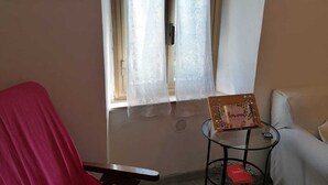 A room with a wooden-framed window, a red chair, a small round table with a book, and a sofa. - La Casetta di Mimmi (Castel Viscardo)
