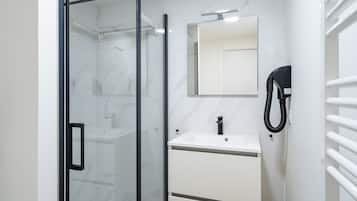 Un baño moderno con cabina de ducha de vidrio, un lavabo blanco con espejo y un perchero en la pared.