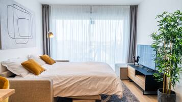 A modern hotel room with a bed, a desk, a television, and a large window with curtains.
