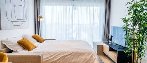 A modern hotel room with a bed, a desk, a television, and a large window with curtains.