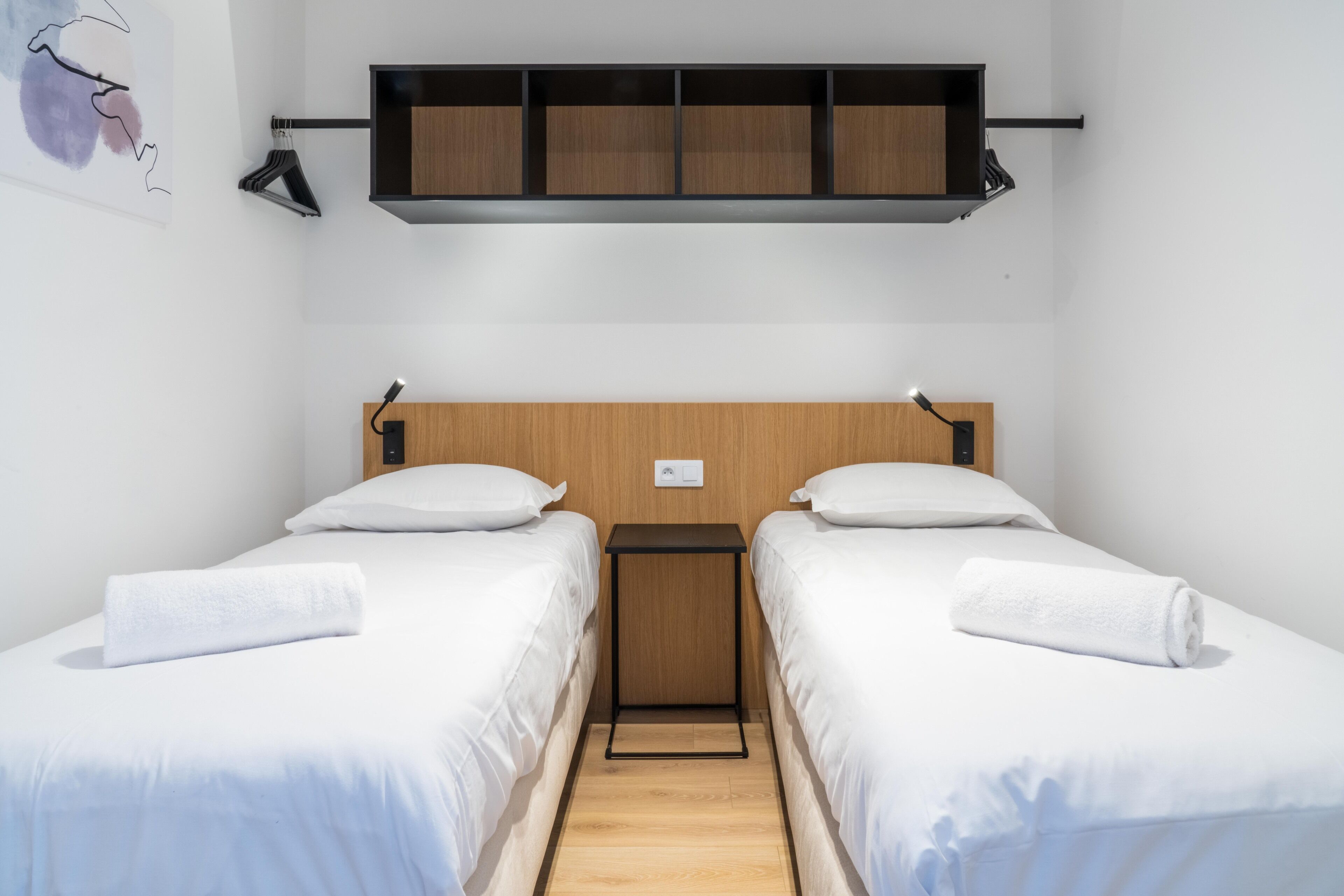 Hotellihuone, jossa on kaksi erillistä sänkyä, puinen pääty, pieni yöpöytä ja hylly sänkyjen yläpuolella.