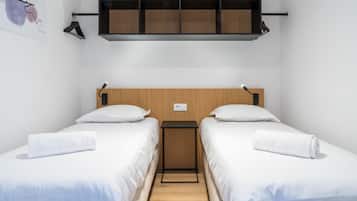 Ett hotellrum med två separata sängar, en sänggavel i trä, ett litet nattduksbord och en hylla ovanför sängarna.