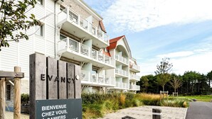 A multi-story hotel with balconies, a sign reading "BIENVENUE CHEZ VOUS, À CAMIERS TRÉSORS D'ORPALE", and a paved walkway. - Evancy Trésors d'Opale (Camiers)