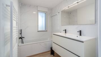 Une salle de bain moderne avec une baignoire, deux lavabos, un grand miroir et une fenêtre.