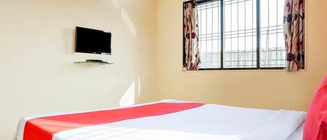 Une chambre d’hôtel avec un lit, un téléviseur à écran plat fixé au mur et une fenêtre avec des rideaux.