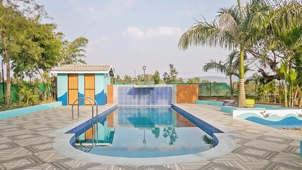 A swimming pool with a tiled deck, a small building with a tiled roof, and palm trees. -  Royal Hills Resort (Mawal)
