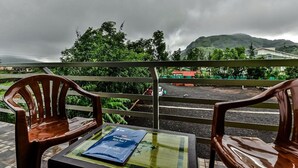 A balcony with two wooden chairs and a table, overlooking a road and greenery with a mountain in the background. -  Royal Hills Resort (Mawal)