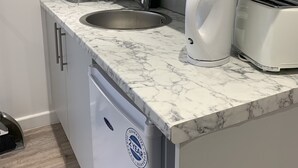 A modern kitchen with a marble countertop, stainless steel sink, white cabinets, and a built-in dishwasher. - Wagtail Way Kent (Orpington)