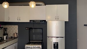 Una cucina moderna con mobili bianchi, un frigorifero in acciaio inox, un piano cottura a gas e lampade a sospensione.