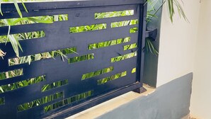 Un balcone con erba sintetica, un recinto in metallo nero e vista su aree verdi e edifici sullo sfondo.