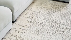 Un soggiorno moderno con un divano angolare grigio, cuscini decorati, una coperta bianca e un tappeto a motivi.