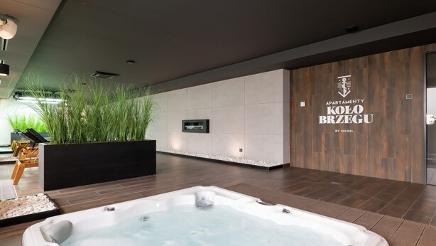 A modern indoor spa area with a hot tub, wooden flooring, and a wall-mounted TV.