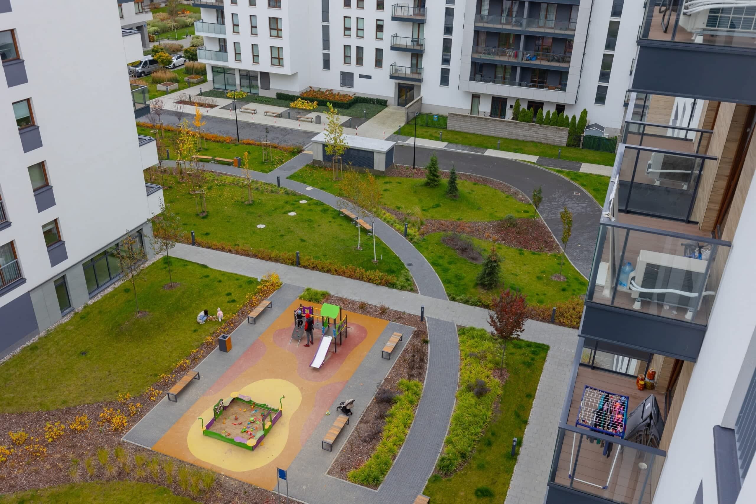 A modern apartment complex with a central courtyard featuring a playground, benches, and a walking path.