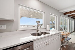 A modern kitchen with a large window, a stainless steel sink, and a view of the beach.