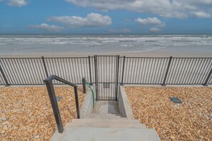 Una scala conduce a una spiaggia, con ringhiera metallica e ciottoli.