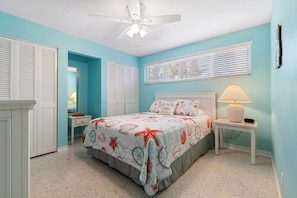 A bedroom with a bed, a nightstand, a lamp, a ceiling fan, and a window with blinds.
