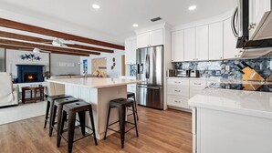 A modern kitchen with white cabinets, stainless steel appliances, and a central island with bar stools. - Ponce Inlet Beach House (Ponce Inlet)