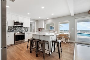 A modern kitchen with white cabinets, a central island with stools, a large window overlooking a pool, and a view of the ocean. - Gorgeous 4 bedroom oceanfront house with pool - Ponce Inlet Beach House (Ponce Inlet)