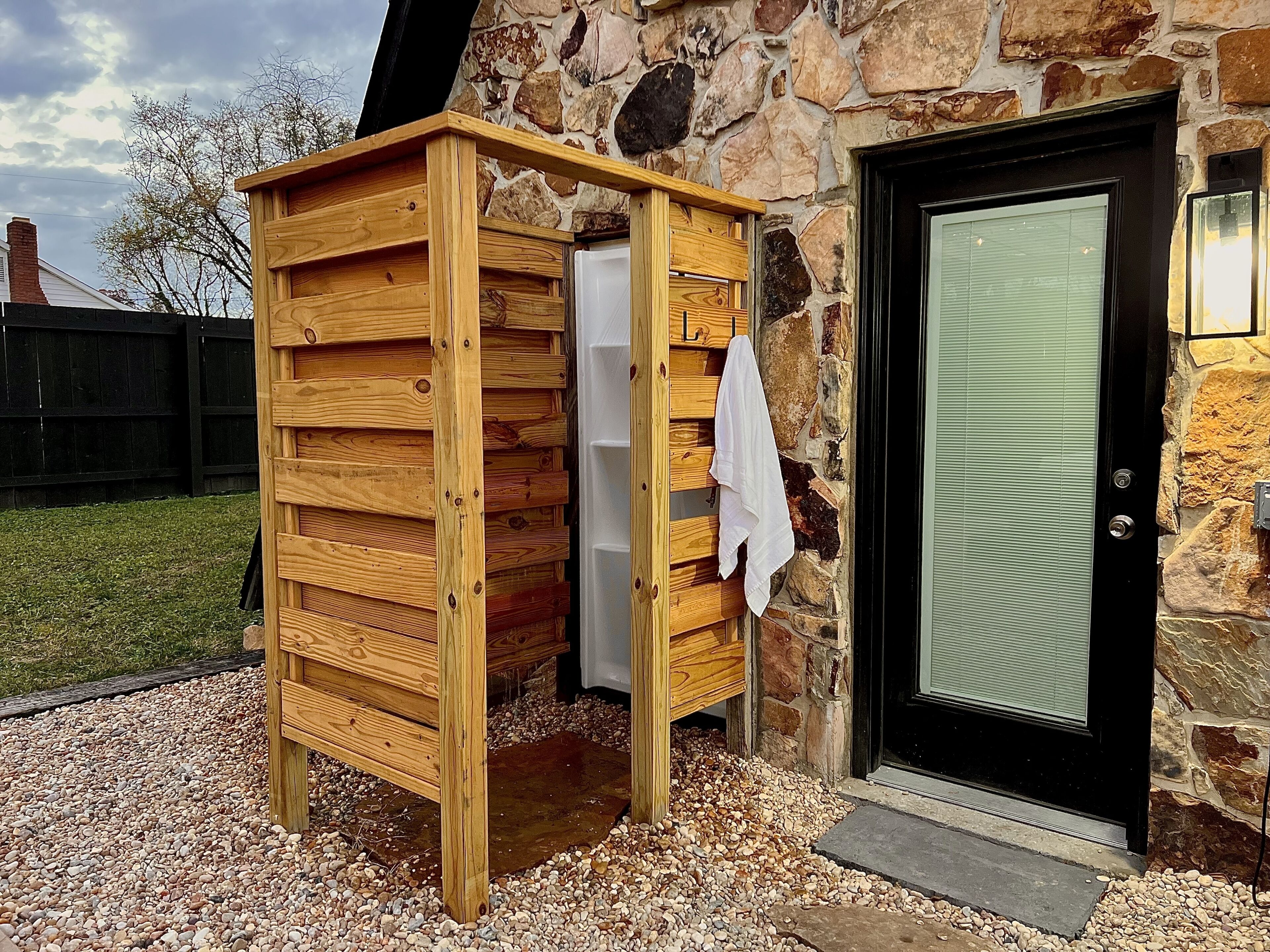 A wooden outdoor shower structure with a stone wall and a door.